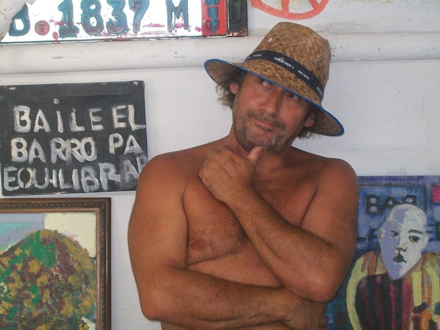 Marcos Shannon en su taller junto a un cartel pintado a mano que dice: baile el barro pa equilibrar